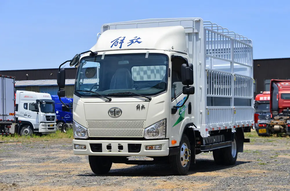 White FAW Jiefang electric light truck with a stake cage cargo body, front and side view, parked outdoors on a gravel lot.