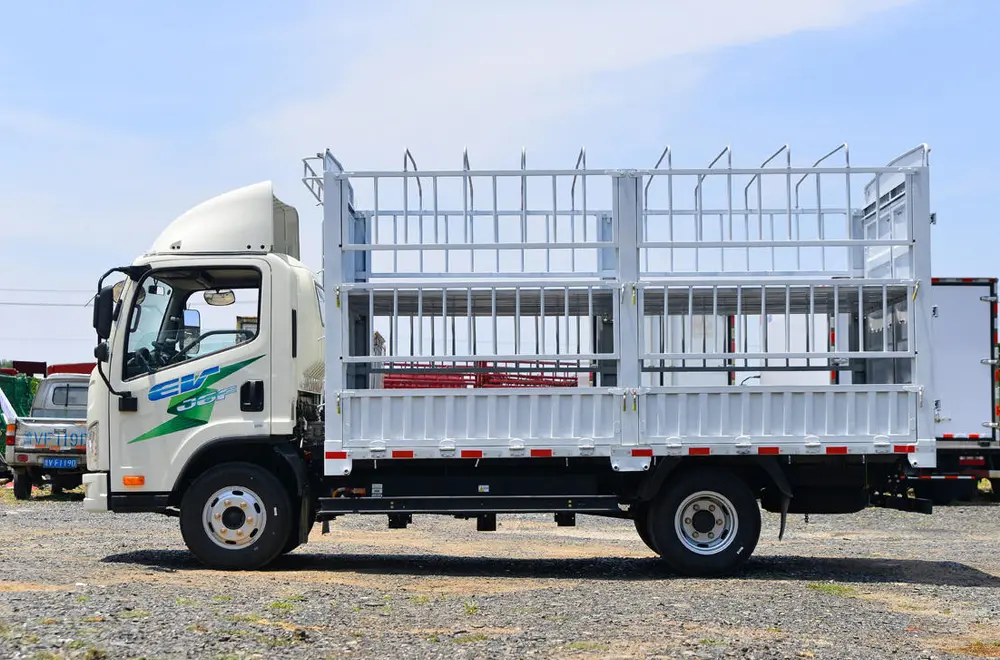 White FAW Jiefang electric light truck with a stake cage cargo body, front and side view, parked outdoors on a gravel lot.